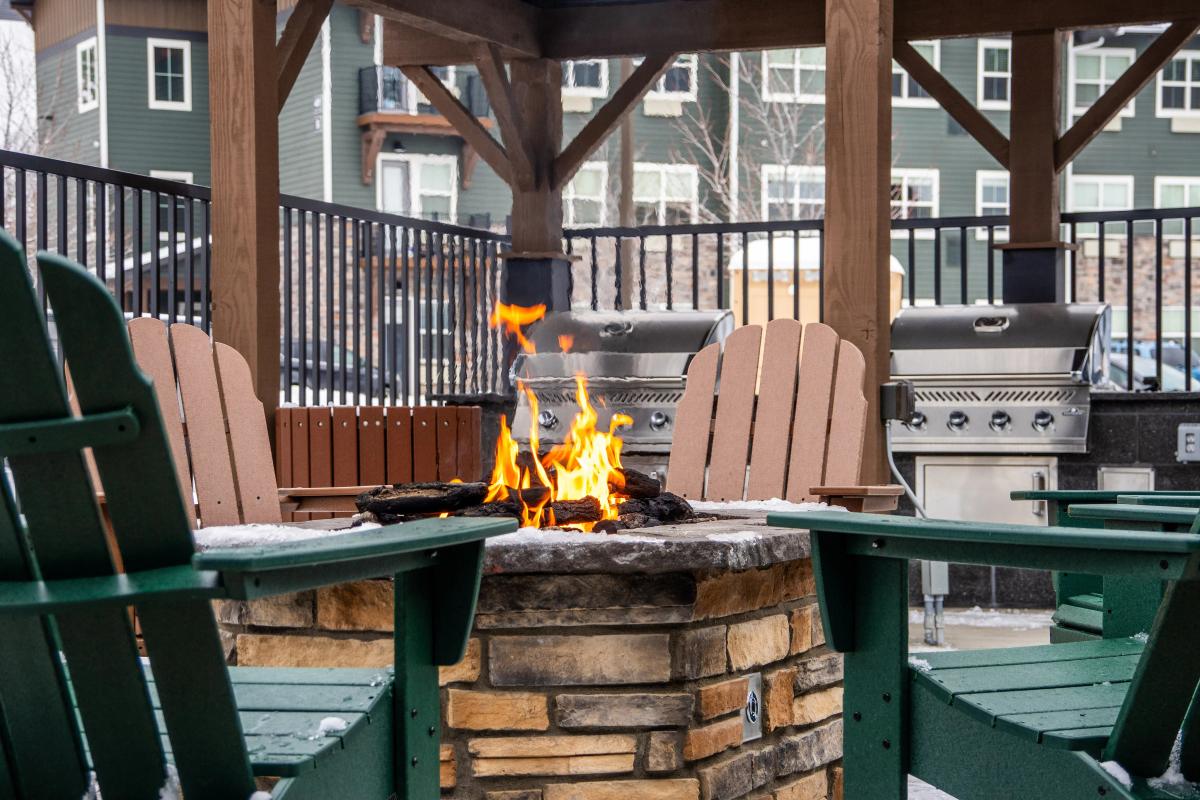 Inviting outdoor patio with a stone fire pit surrounded by wooden Adirondack chairs and barbecue grills.
