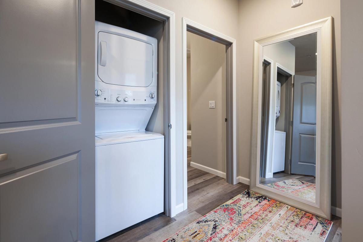 Contemporary apartment hallway featuring a stackable washer and dryer, elegant mirror, and vibrant rug.